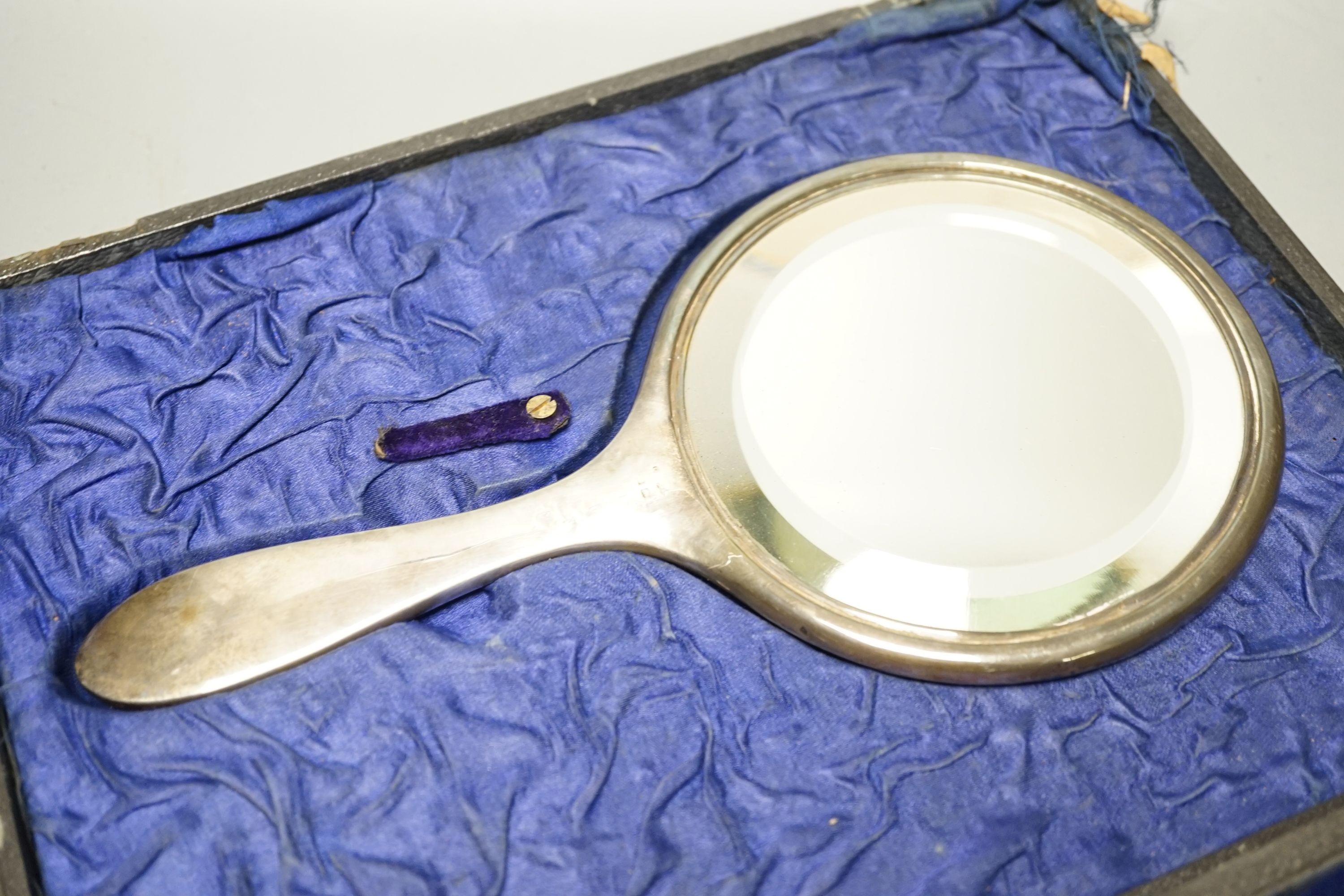A cased George V three piece silver mounted dressing table set, including a mirror and two brushes.